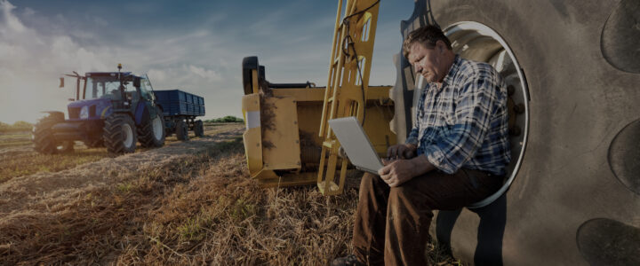 Combine with operator sitting in wheel using a laptop.